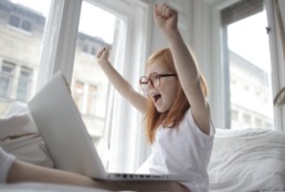 Petite fille qui lève les bras devant son ordinateur en signe de victoire