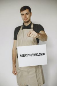 Jeune homme avec un tablier tenant une pancarte "Sorry we're closed"