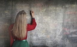 Femme de dos expliquant un problème mathématique sur un tableau en ardoise